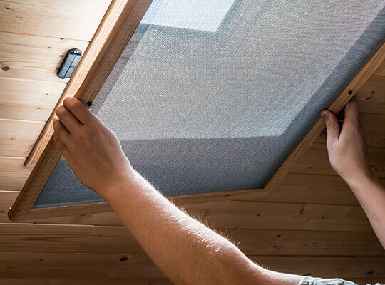 A man installing a screen on a window located on the ceiling.